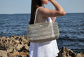 Bolso Ombak plata artesanal de SAYA llevado por una modelo frente al mar.
