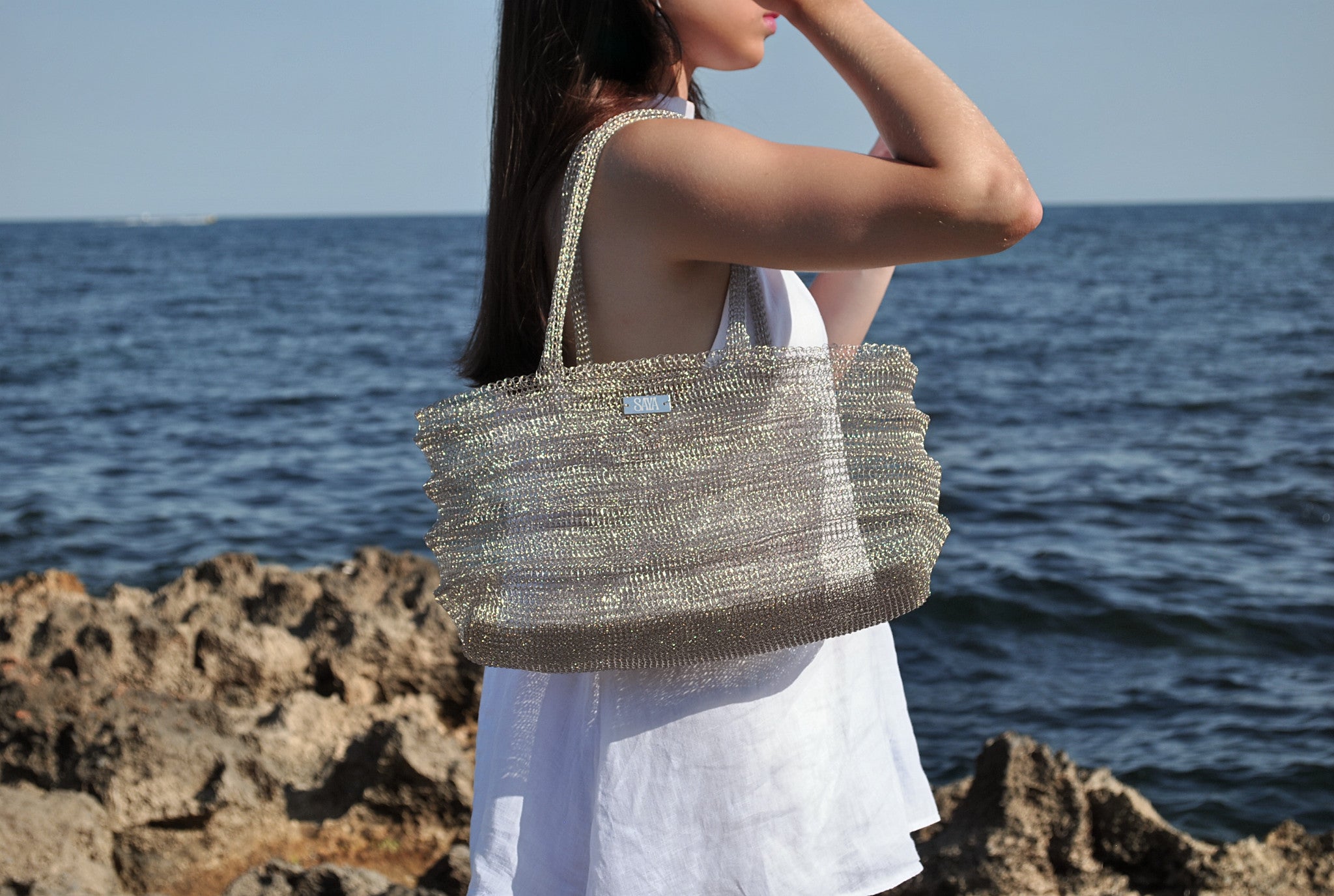 Bolso Ombak plata artesanal de SAYA llevado por una modelo frente al mar.