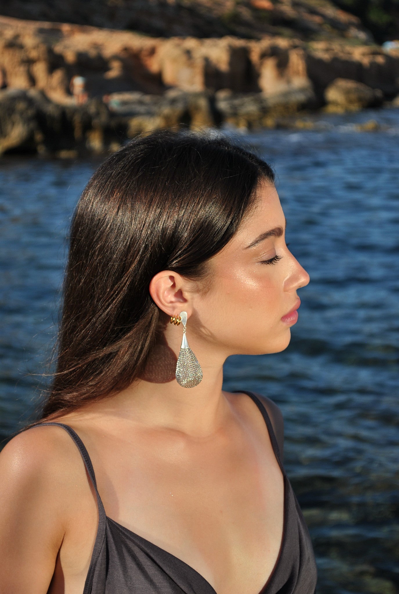 Modelo llevando los pendientes Glop Plata de SAYA tejidos a mano en crochet metálico frente al mar.