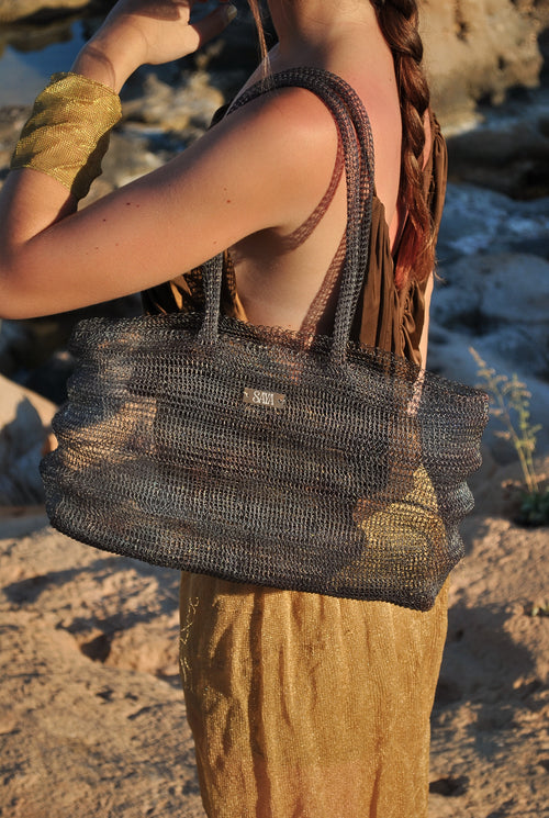 Bolso Ombak negro artesanal de SAYA llevado por una modelo en una cala.