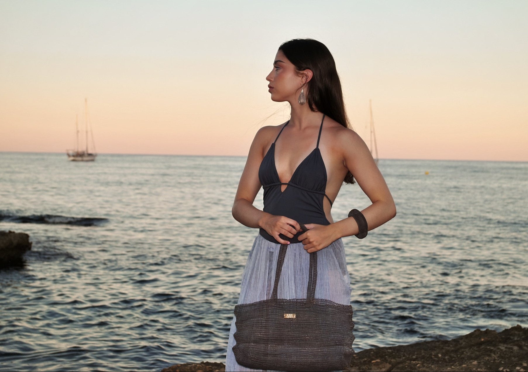 Bolso Ombak negro artesanal de SAYA llevado por una modelo frente al mar.